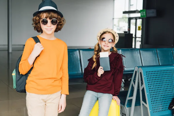Niños preadolescentes lindos en gafas de sol en la sala de espera con mochila, billete de avión y pasaporte - foto de stock