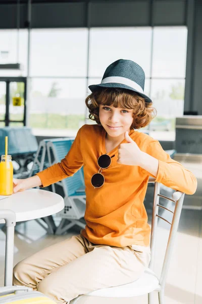 Preadolescente chico mostrando pulgar hacia arriba en el aeropuerto y mirando a la cámara — Stock Photo