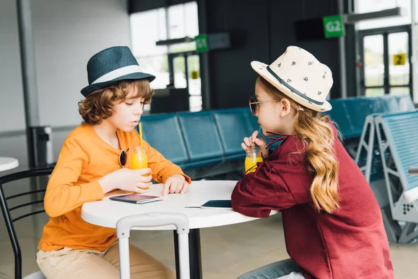 Bambini preadolescenti seduti a tavola con succo d'arancia nella sala partenze — Foto stock