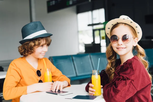 Crianças pré-adolescentes sentadas à mesa com suco de laranja na sala de partida — Fotografia de Stock