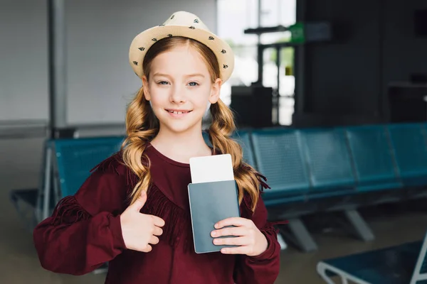 Lindo niño preadolescente con pasaporte y billete de avión que muestra el pulgar en el aeropuerto - foto de stock