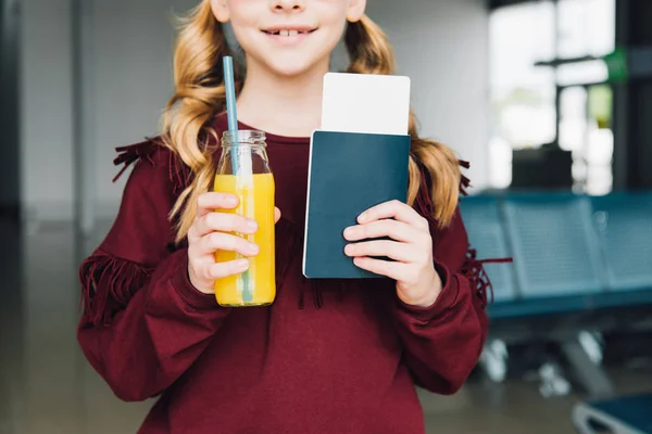 Vista ritagliata del bambino preadolescente con biglietto aereo, passaporto e succo d'arancia in aeroporto — Foto stock