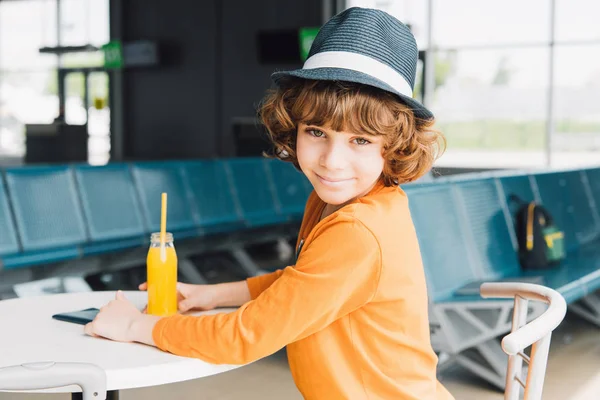 Bonito preteen menino sentado à mesa com suco de laranja no espera hall — Fotografia de Stock