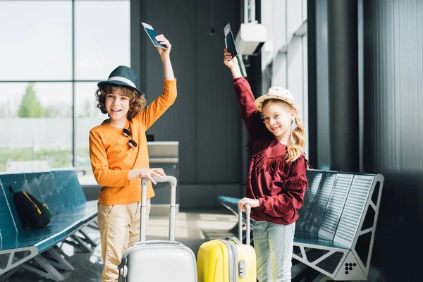 Niños preadolescentes felices con maletas, billetes de avión y pasaportes en la sala de espera - foto de stock