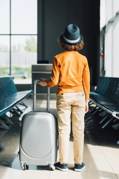 Вид ззаду хлопчика з валізою в залі очікування в аеропорту — стокове фото