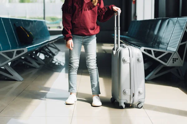 Cropped view of preteen kid with suitcase in waiting hall in airport — Stock Photo