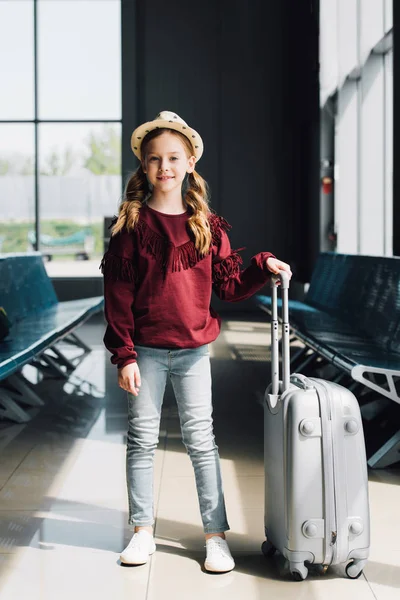 Smiling preteen kid with suitcase in waiting hall in airport — Stock Photo