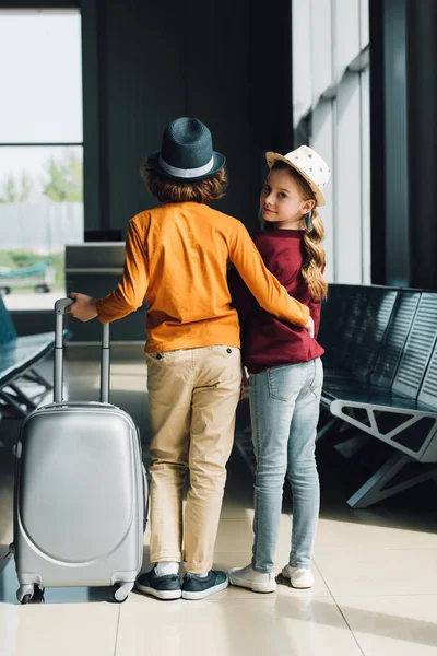 Вид ззаду хлопчика з валізою, що обіймає хлопчика в залі очікування — стокове фото