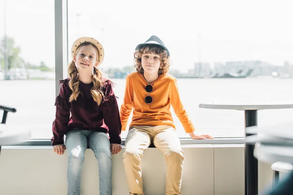 Adorable préadolescent enfants assis sur la fenêtre pendant la journée et regardant la caméra — Photo de stock