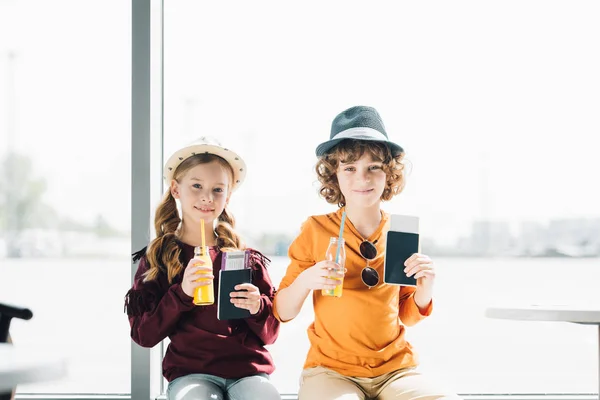 Cute preteen kids in waiting hall in airport with passports, air tickets and orange juice — Stock Photo