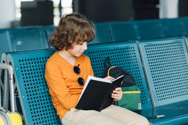Preteen kid sitting in waiting hall and writing in notebook — Stock Photo