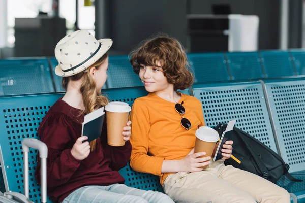 Lindos niños preadolescentes sentados en la sala de espera con café para llevar y pasaportes - foto de stock