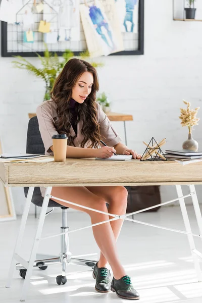 Attraktive Frau schreibt am Notizbuch, während sie beim Coffee to go sitzt — Stockfoto