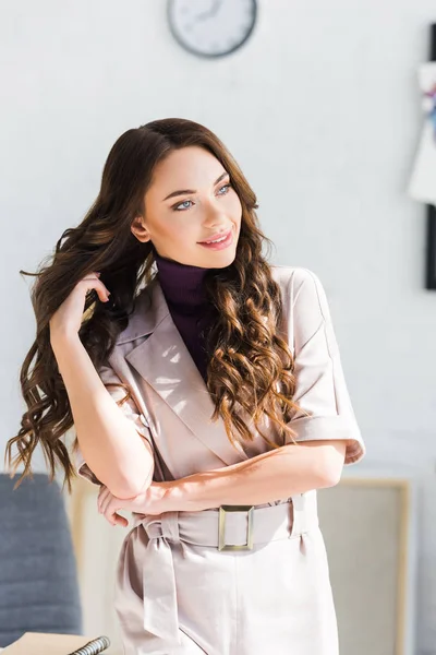 Feliz chica rizada sonriendo mientras está de pie y tocando el cabello - foto de stock