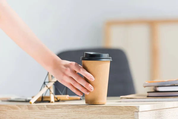 Cropped view of woman holding coffee to go near stationary and notebooks — Stock Photo