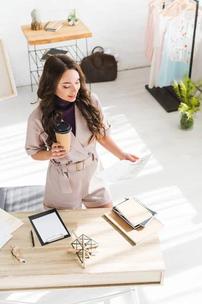 Overhead view of cheerful girl holding paper cup and fashion sketches — Stock Photo