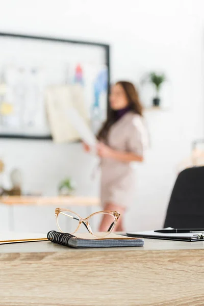 Selective focus of glasses near notebook and pen on wooden table near girl — Stock Photo