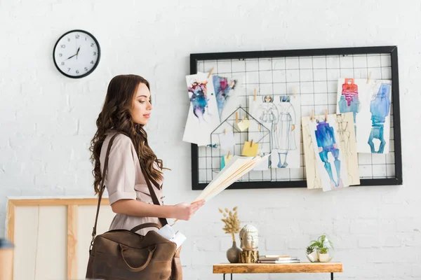 Attraktive junge Designerin mit Tasche in der Nähe von Modeskizzen — Stockfoto