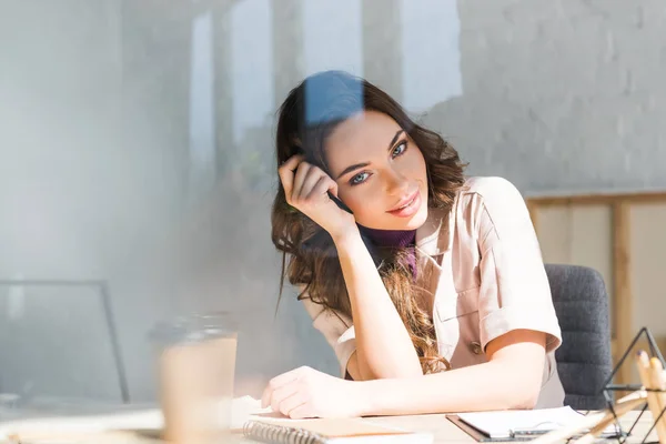 Selektiver Fokus eines fröhlichen Mädchens, das neben Schreibtisch und Pappbecher auf dem Tisch sitzt — Stockfoto