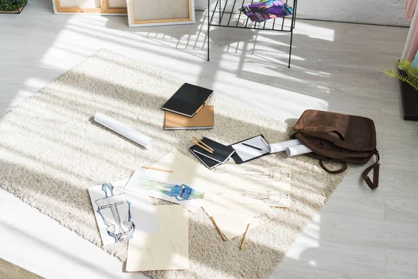 Notizbücher und Modeskizzen auf Teppich neben Tasche und Klemmbrett — Stockfoto