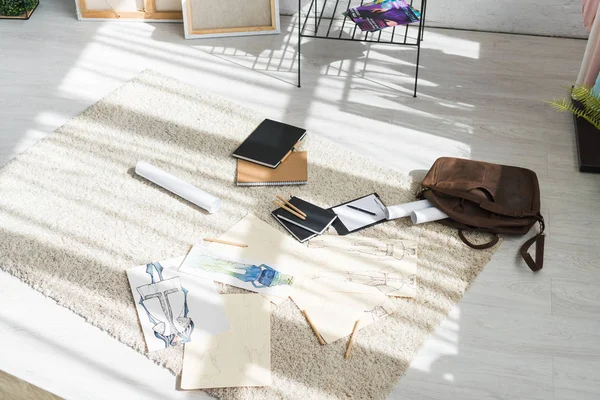 Cuadernos y bocetos de moda en la alfombra cerca de la bolsa y portapapeles - foto de stock