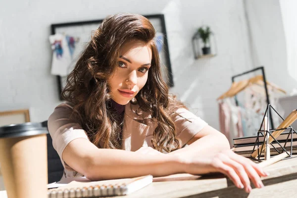 Selective focus of serious and beautiful curly young woman near paper cup — Stock Photo