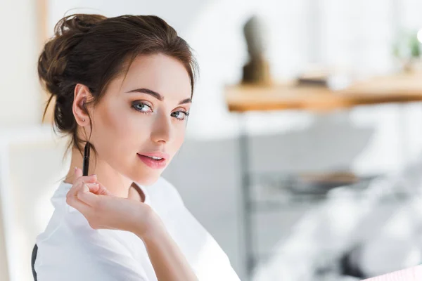 Attraktive junge Frau im weißen T-Shirt blickt in die Kamera, während sie den Stift in der Hand hält — Stockfoto