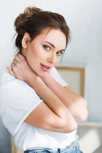 Schöne junge Frau im weißen T-Shirt, die in die Kamera schaut und den Hals berührt — Stockfoto