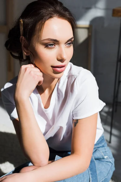 Mujer joven pensativa en camiseta blanca pensando en casa - foto de stock