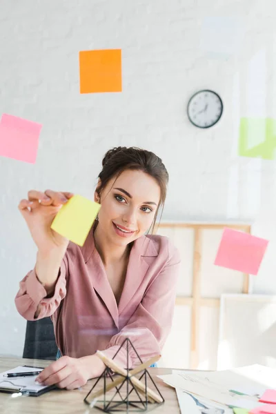 Attractive young woman hanging sticky note on window — Stock Photo