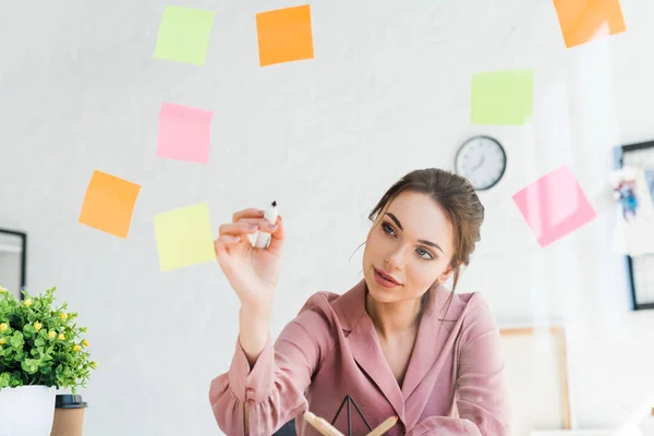 Attractive young woman writing on window with sticky notes — Stock Photo