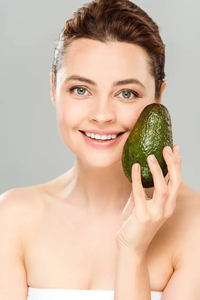 Усміхнена приваблива жінка тримає органічне і стигле авокадо ізольовано на сірому — стокове фото