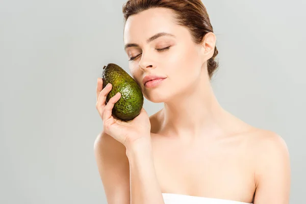 Приваблива жінка з закритими очима тримає стигле авокадо ізольовано на сірому — стокове фото