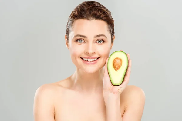 Весела гола жінка тримає половину органічного і стиглого авокадо ізольовано на сірому — стокове фото