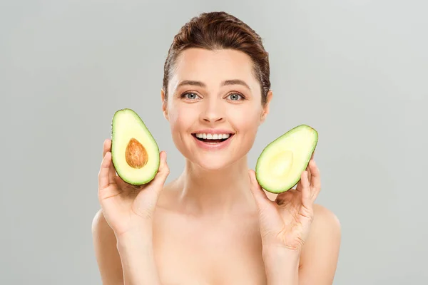 Mujer desnuda feliz sosteniendo mitades de aguacate orgánico aislado en gris - foto de stock