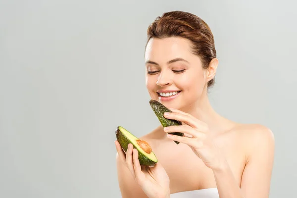 Happy woman holding halves of organic avocado isolated on grey — Stock Photo