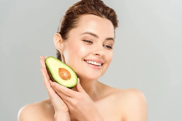 Mujer feliz y desnuda sosteniendo la mitad del aguacate maduro aislado en gris - foto de stock