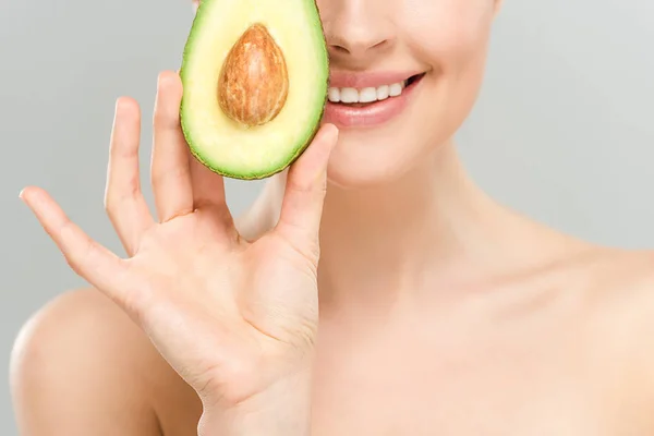 Обрізаний вид на голу усміхнену жінку, що тримає половину смачного авокадо ізольовано на сірому — стокове фото