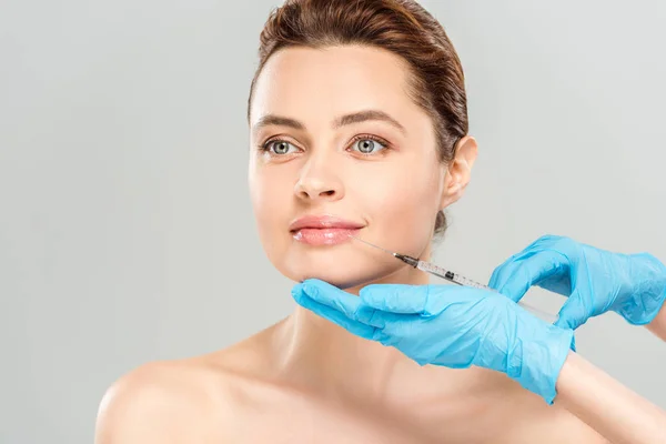 Vista recortada del cosmetólogo en guantes de látex azul sosteniendo la jeringa cerca de la cara de la mujer desnuda aislada en gris - foto de stock