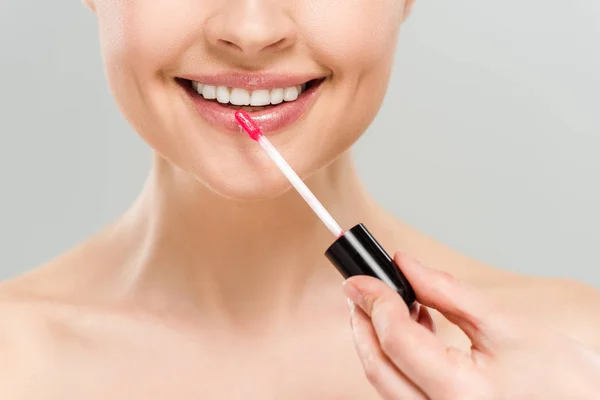 Vista recortada de mujer desnuda alegre aplicando brillo de labios y sonriendo aislado en gris - foto de stock