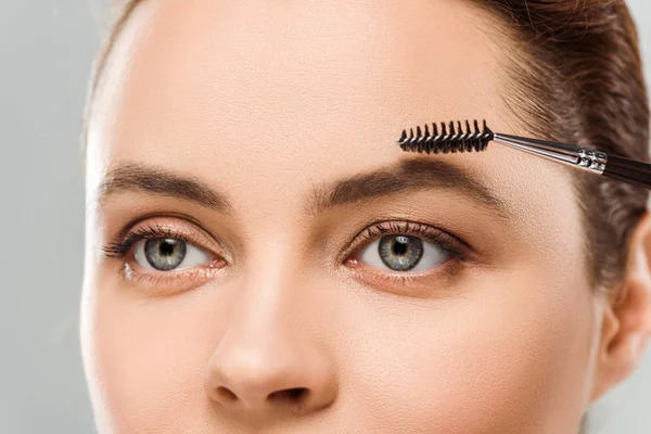 Cropped view of woman shaping eyebrow with eyebrow brush isolated on grey — Stock Photo