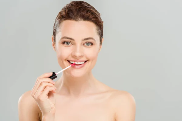 Cheerful naked woman applying lip gloss on lips isolated on grey — Stock Photo