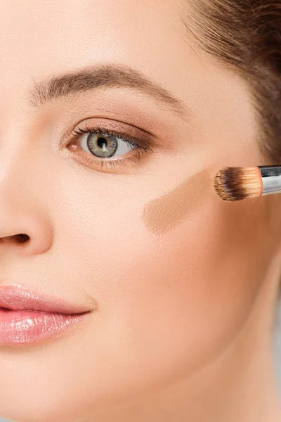 Cropped view of woman holding cosmetic brush and applying brown blush on cheek isolated on grey — Stock Photo