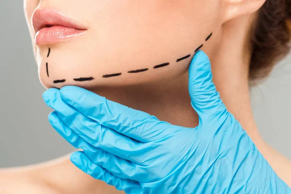 Abgeschnittene Ansicht eines plastischen Chirurgen, der das Gesicht einer Frau mit markantem Gesicht berührt, isoliert auf grau — Stockfoto