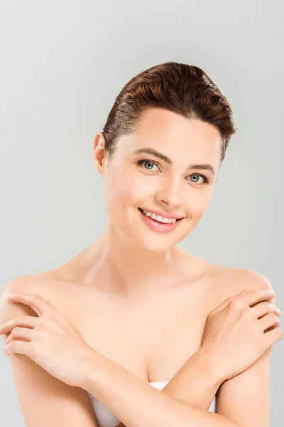 Cheerful woman touching shoulders and smiling isolated on grey — Stock Photo