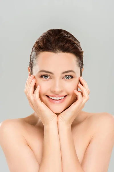 Atractiva mujer sonriendo mientras toca la cara aislada en gris - foto de stock