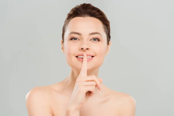 Mujer alegre mostrando signo de silencio y sonriendo aislado en gris - foto de stock