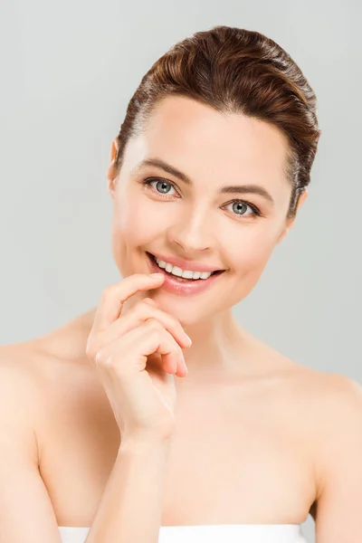 Positive woman looking at camera and touching face isolated on grey — Stock Photo