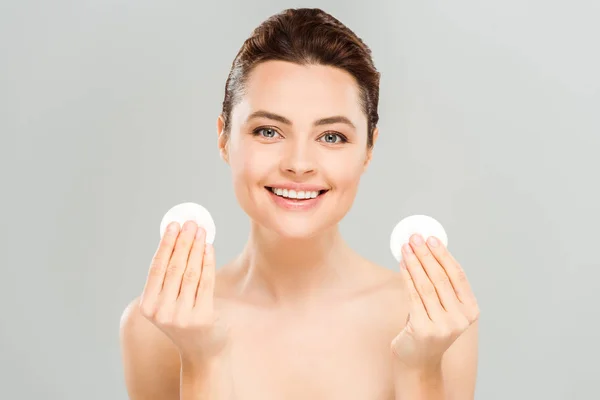 Mujer positiva y desnuda sosteniendo almohadillas de algodón y sonriendo aislada en gris - foto de stock