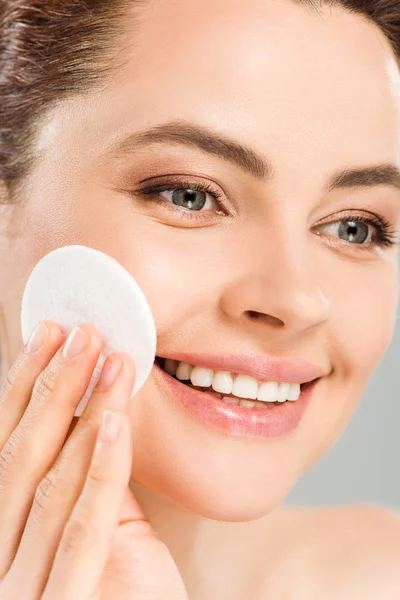 Close up of cheerful woman holding cotton pad near face isolated on grey — Stock Photo